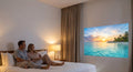 Couple watching a beach film projected on a hotel room wall at night with the INNOVATIVE K5x travel projector